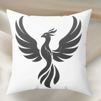 A square white throw pillow featuring a large black phoenix graphic printed on the front, displayed against a soft beige fabric background.
