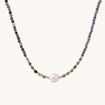 Delicate beaded necklace with violet iolite stones, gold spacers, and central white freshwater pearl on neutral background.