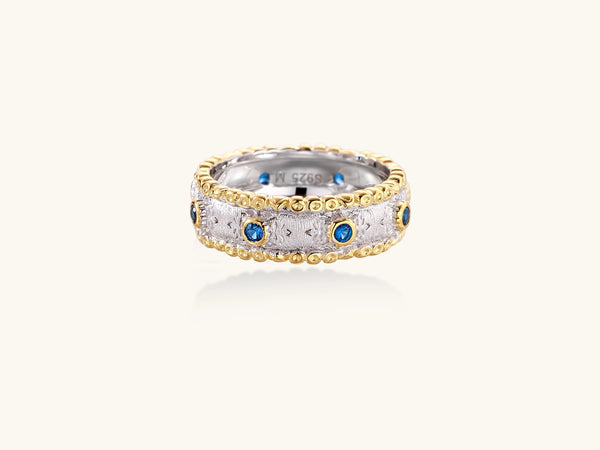 Sterling silver ring with brushed center band, blue zirconia stones, and 24k gold-plated decorative borders.