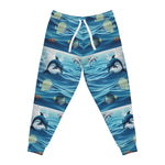 Blue patterned jogger pants featuring an all-over print of dolphins jumping in the ocean, tropical fish, and white drawstrings at the waist, shown on a plain white background.