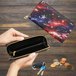 A zip-around wallet shown open in hands over a wooden surface, with its closed counterpart displayed above. The wallet has a black interior and a galaxy print exterior in red, blue, and purple with white stars.