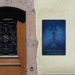 Decorative metal sign with blue design and text on a stone wall next to a wooden door.