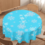 Round table with a blue tablecloth featuring white snowflake patterns in a room with wooden floor and furniture.