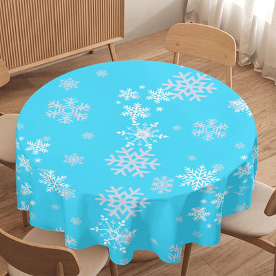 Round table with a blue tablecloth featuring white snowflake patterns in a room with wooden floor and furniture.