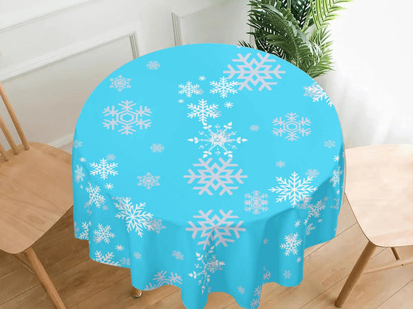 Round table with a blue tablecloth featuring white snowflake patterns, placed in a room with wooden floor and chairs.