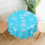 Round table with a blue tablecloth featuring white snowflake patterns, placed in a room with wooden floor and chairs.