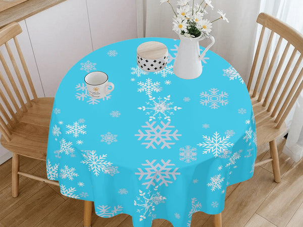 Round table with a blue tablecloth featuring white snowflakes, surrounded by wooden chairs in a room.