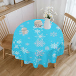 Round table with a blue tablecloth featuring white snowflakes, surrounded by wooden chairs in a room.