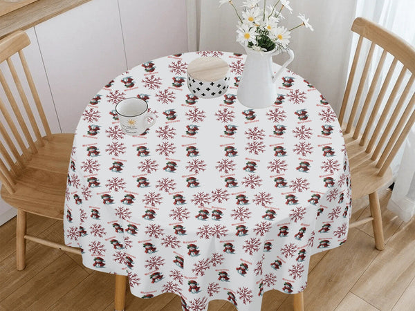 Round table with a decorative tablecloth featuring penguin and snowflake pattern, wooden chairs, and a vase with flowers in the background.