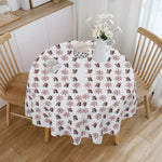 Round table with a decorative tablecloth featuring penguin and snowflake pattern, wooden chairs, and a vase with flowers in the background.
