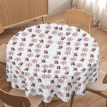 Round table with a festive tablecloth featuring snowmen and snowflakes in a room with wooden furniture.