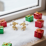 Gold and silver rose cross earrings with miniature gift boxes on a snowy surface.