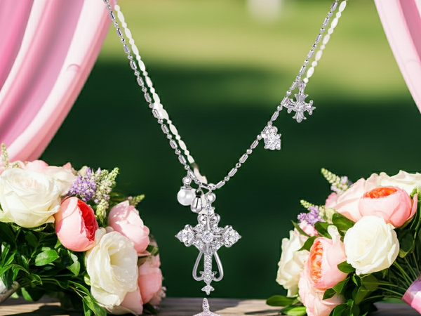 Silver cross necklace over a stand with pink and white flowers in the background