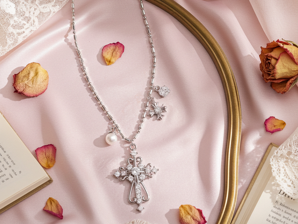 Silver necklace with a cross pendant on a pink fabric background with dried flowers and lace.