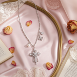 Silver necklace with a cross pendant on a pink fabric background with dried flowers and lace.