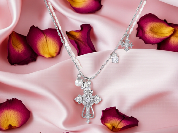 Silver necklace with a cross pendant on pink fabric with purple flower petals