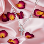 Silver necklace with a cross pendant on pink fabric with purple flower petals