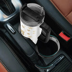 White mug with gold stars in a black cup holder inside a car.