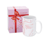 White mug with pink floral design next to a pink gift box with a red ribbon on a white background