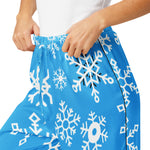 Blue pajama pants with white snowflake patterns worn by a person on a white background