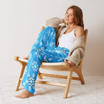 Woman sitting on a wooden chair wearing blue snowflake pajama pants and a beige cardigan.
