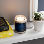 Candle in a glass jar with a blue label on a shelf next to books and a plant