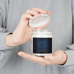 Person holding a candle jar with a label featuring text and a design.